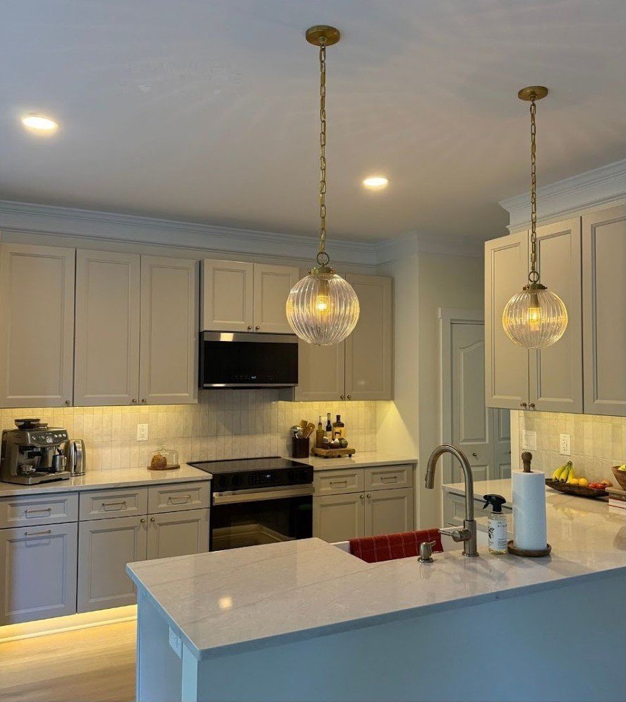 Kitchen after — glass pendant lights over the island, under-cabinet lighting, and recessed cans